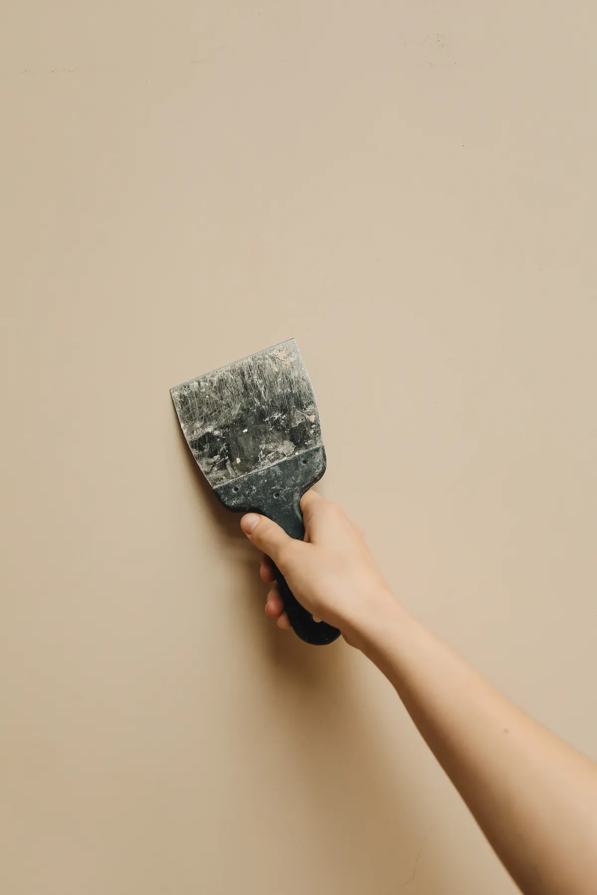A hand using a putty knife to smooth a wall