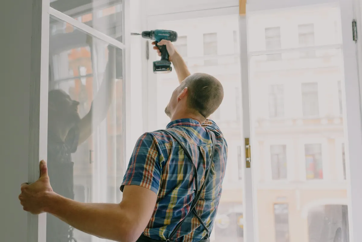 A worker adjusting a window frame with a cordless drill